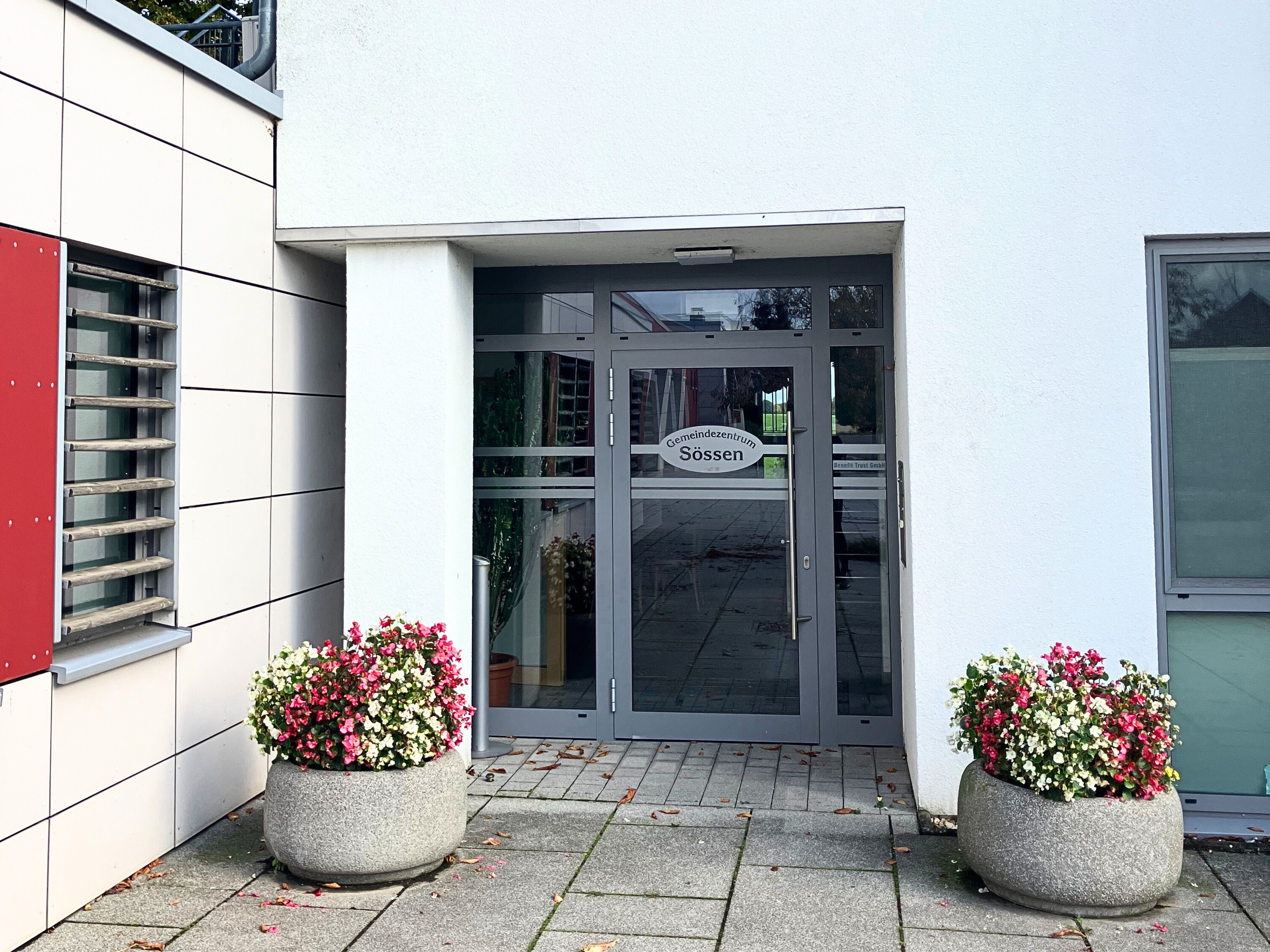 Eingangstür des Gemeindezentrum Sössen in Lützen gerahmt von zwei steinernen Blumenkübeln mit rot-weißen Blumen